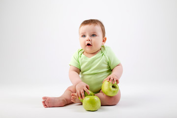 Fototapeta premium Cute toddler in green bodysuit sits with green apples on white background