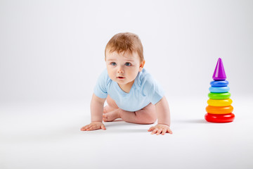 Cute baby in blue bodysuit plays with multi-colored pyramid on a white background, space for text