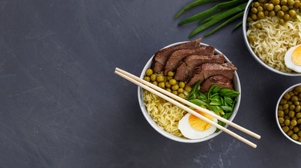Asian traditional soup in a bowl on grey background. Beef pho bo with eggs and green peas. Copy...