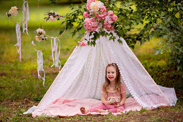 Fototapeta na wymiar Portrait of a cute happy little girl 3-4 years old in the summer in the park in an openwork floral wigwam.