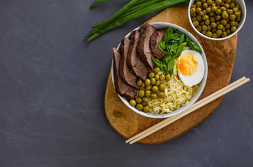 Asian traditional soup in a bowl on grey background. Beef pho bo with eggs and green peas. Copy space.