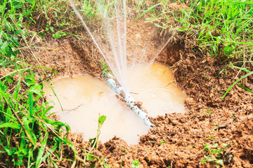 broken leak pvc water pipe busting with water leakage, under hole dirt in ground, representing broken disruptive explosion, water spraying out chaotically, plumbing construction fixing repairing