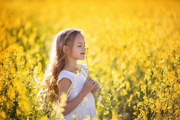 Naklejka na ściany i meble Portrait of a cute happy little girl 5-7 years old in nature, in the summer in a rape field.