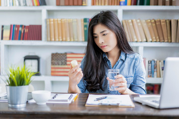 Asian beautiful woman raking tablet medicine from hard long work stress tired for pain relief working from home office in isolation quarantine, using computer laptop planning strategy business company