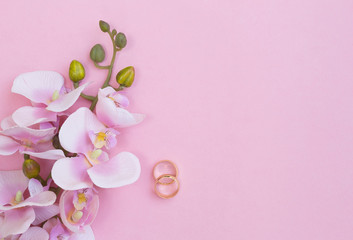 Pink orchids and two golden wedding rings on pink background. Top view.