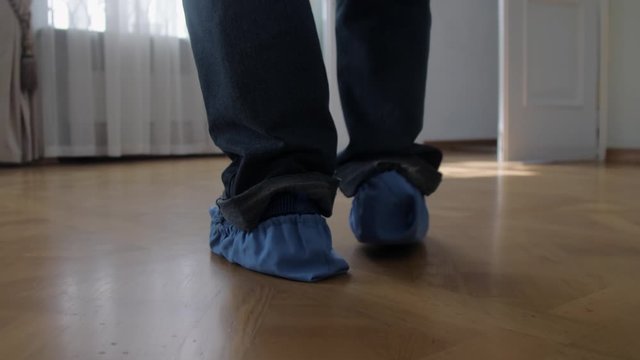 man legs in jeans and blue shoe covers walk along clean parquet floor leisurely in museum close view slow motion. Concept historical heritage excursion
