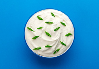 Bowl of sour cream on blue background, top view