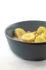 a blue ceramic bowl filled with fruit muesli with extra banana pieces. The bowl is focused isolated on a white background