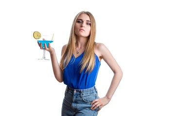 A girl looks haughty in bright blue jeans and a blouse with a blue cocktail with lemon. Young lady resting with alcohol