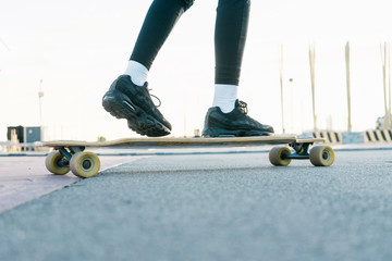 Unrecognizable woman rides on longboard around sunlit park.