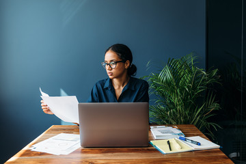 Serious businesswoman sitting by a desk and holds documents