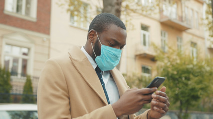 Young African American man wearing face mask look around use phone on street coronavirus safety protection pandemic outbreak medical mask slow motion