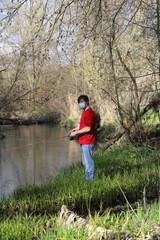 a masked man on a river fishing during quarantine, a violation of self-isolation during the coronavirus pandemic