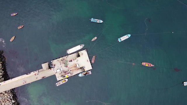 Aerial drone footage of fishermen pier and moored fishing boats. Directly above drone view of small fishing village. Los Lagos, Bahia, Mansa, Pacific coast, Chile.