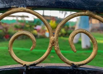Old golden metal design and green garden behind it.