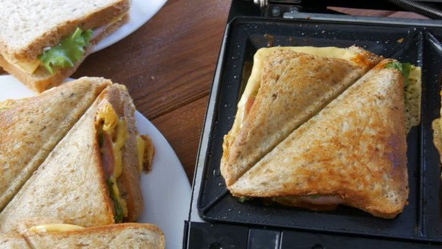 Morning breakfast in the home kitchen. Sandwiches with bacon, cheddar cheese and lettuce are fried in a special toaster or a sandwich maker. Special kitchen spatula takes fresh sandwich bread.