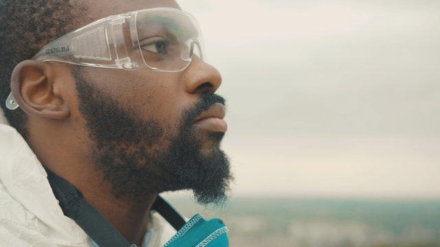 African american young man in chemical protection suit wearing face respirator mask standing on mountain top. Ecology disaster. Save the environment. Pandemic. Coronavirus.