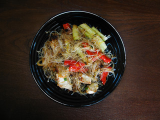funchosa with chicken fillet, carrots, bell peppers, fresh cucumbers, green onions, soy sauce, teriyaki sauce and sesame. cellophane noodles on a black plate. the view from the top.