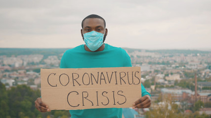 Angry strong african unemployed man fighting against job loss showing Coronavirus Crisis banner shouting call outs on mountain top. Pandemic. Glonal unemployment.