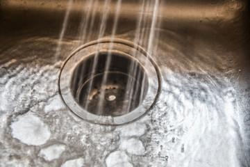 Monochromatic water spraying into a garbage disposal in stainless steel sink with water and bubbles pooling and running on surface - some grain and movement blur from water