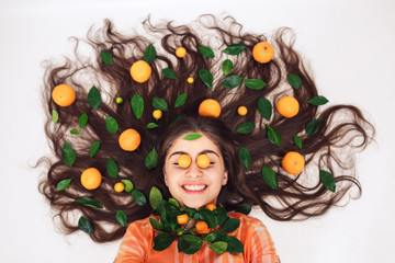 girl with curly hair in an orange shirt, with tangerines in her hair. hair and skin care concept