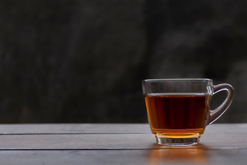 Close up hot tea cup on wood table . hot tea in handle glass with copy space for text or design. Hot tea with raw mortar background.
