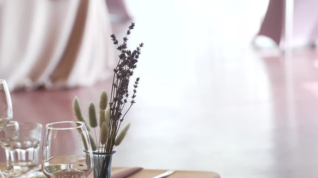 Wildflowers, lagurus and lavender stand in a glass vase on a festive table on a pink tablecloth near a glass goblet