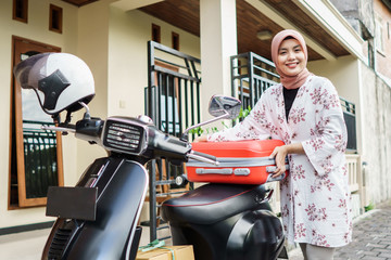 attractive muslim woman traveling with motorbike carrying suitcase. eid mubarak holiday trip