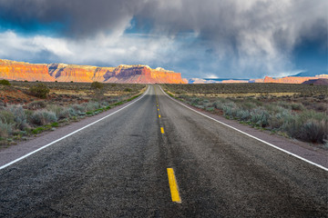 Fototapeta premium The road running through the dry prairie and rests on the red mountains on the background of a stormy sky.