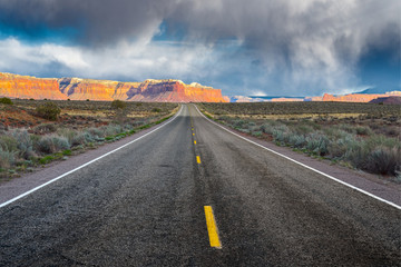 The road running through the dry prairie and rests on the red mountains on the background of a stormy sky.