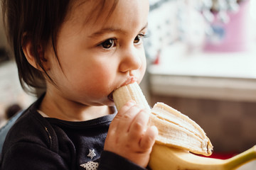 Cute baby eating banana. Cute little girl eating fruit. Healthy snack, food