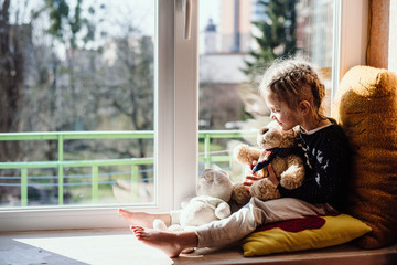 Cute little girl enjoying the sunshine while sitting at the window. The child looks out the window...