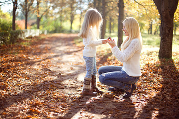 Beautiful, happy young mother with little daughter playing in Autumn park.