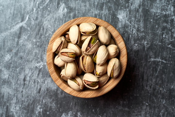 Wooden bowl with pistachios on a dark background.