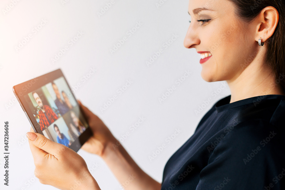 Wall mural App for video call at digital tablet. A girl is holding a tablet in hands and talking online with a few friends together