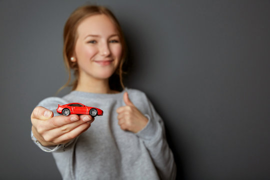 Idea and concept for the driving school, learner driver has passed the test, driving licence, portrait of an authentic and beautiful young woman, teenager holding a car in her hand