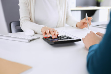 Accountant checking financial statement or counting by calculator income for tax form, hands closeup. Business woman sitting and working with colleague at the desk in office toned in blue. Tax and