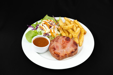 Grilled ham steak with barbecue sauce, side dish salad and french fries on sackcloth. Copy space - Black background 