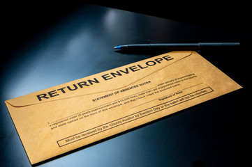 brown absentee ballot return envelope on a black desk with ink pen