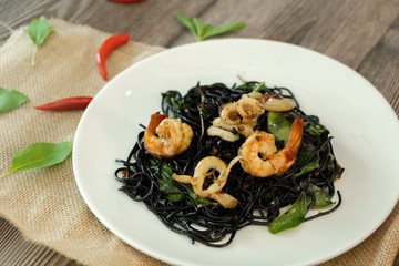 Black spaghetti. Spicy Black seafood pasta with shrimp and octopus with basil over sackcloth wooden table. Mediterranean delicacy food. Copy Space