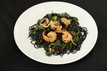Black spaghetti. Spicy Black seafood pasta with shrimp and octopus with basil over black background . Mediterranean delicacy food. Copy Space