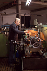 A man 50-60 le works at the machine at the factory. Man with glasses. Hard work.