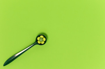 Spoon with organic pills on green background. Medicine dose of nutritional supplements or prescription drugs
