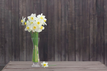 A bouquet of narcissus in a glass vase on a wooden background. Spring time, rustic vibes