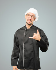 Happy young chef making a gesture of calling with the hand