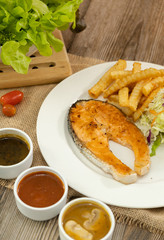 Grilled salmon steak with french fries and fresh salad on sackcloth and wooden table background. Ready to eat food. Copy space.