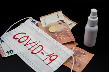 White surgical mask with covid word written on red, euro banknotes and bottle of disinfectant. Concept pandemic crisis of covid.