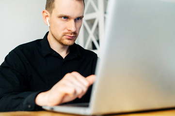 Close up a guy in black shirt using laptop for work, he is watching concentrated on laptop screen. Web browsing, development