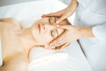 Fototapeta na wymiar Beautiful happy woman enjoying facial massage with closed eyes in spa salon. Relaxing treatment in medicine and Beauty concept