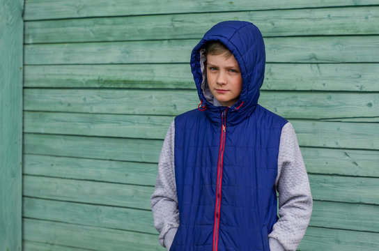 Funny handsome teenage boy is posing for camera. Outdoor portrait of a teenage boy on green background. Expressive boy with a hood on his head